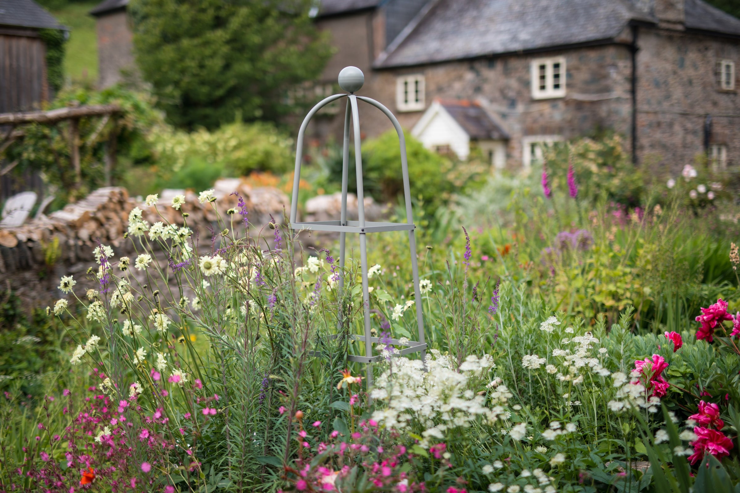 Agriframes classic square obelisk in sage green in a flowerbed in front of a cottage